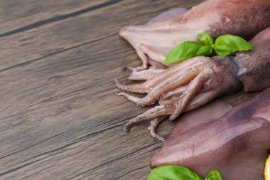 Ahşap masada çiğ kalamar ve fesleğen, yakın plan. Metin için boşluk