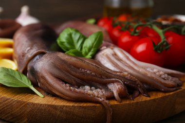 Raw squids, tomatoes and basil on wooden table, closeup