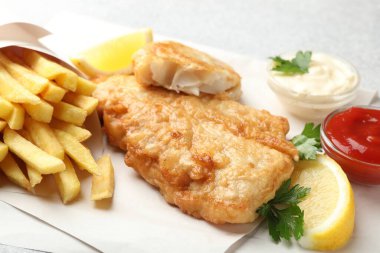 British Traditional Fish and chips served with sauces on light grey table, closeup
