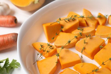 Pieces of fresh pumpkin with thyme in baking dish and ingredients on white table, closeup
