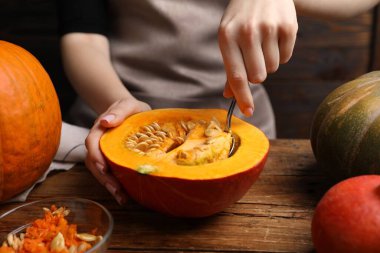 Tahta masada çiğ balkabağından tohum çıkaran kadın, yakın plan.