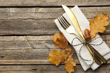 Beautiful table setting. Cutlery with napkin and autumn decor on wooden background, top view. Space for text