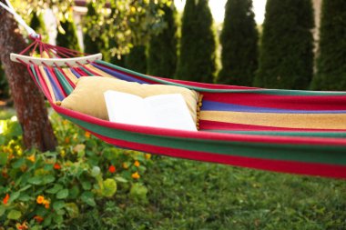 Cushion and book on hammock in garden, closeup