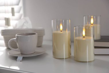Decorative LED candles, tea, books and tissues on white table indoors, closeup