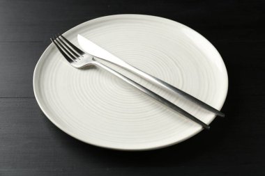 Clean ceramic plate and cutlery on black wooden table, closeup