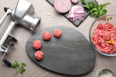 Raw meatballs, ground meat, parsley, onion and grinder on grey table, flat lay