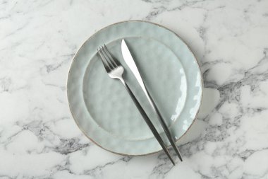 Ceramic plate and cutlery on white marble table, top view