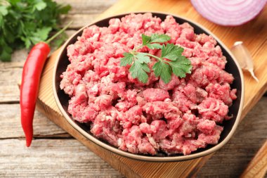 Raw minced meat with parsley and chili pepper on wooden table, closeup