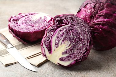 Whole and cut red cabbages with knife on grey table, closeup