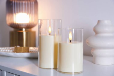 Decorative LED candles, vase, lamp and jewellery on white cabinet indoors, closeup