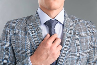 Takım elbiseli adam kravatını gri arka planda düzeltiyor.