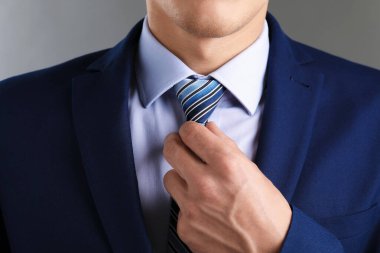 Takım elbiseli adam kravatını gri arka planda düzeltiyor.