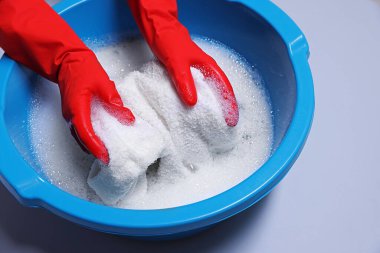 Elbiseleri açık gri arka planda plastik leğende yıkayan kadın, yakın plan.
