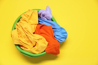 Plastic basin with clothes on yellow background, top view. Space for text