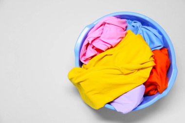 Plastic basin with clothes on light grey background, top view. Space for text