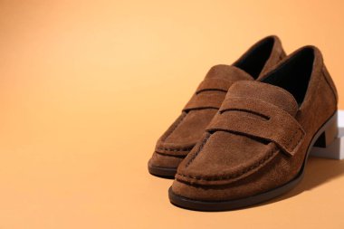 Pair of stylish brown shoes on pale orange background, closeup. Space for text