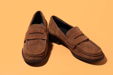 Soluk turuncu arka planda bir çift şık kahverengi ayakkabı, yakın plan.