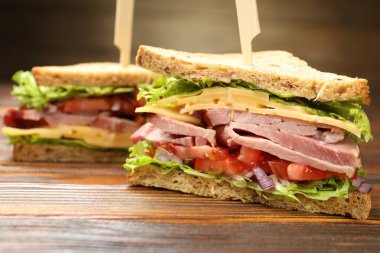 Delicious sandwiches with ham, cheese and vegetables on wooden table, closeup