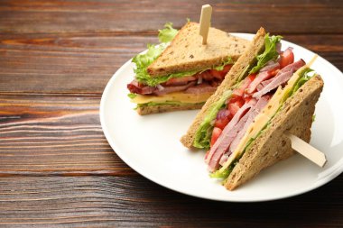 Delicious sandwiches with ham, cheese and vegetables on wooden table, closeup