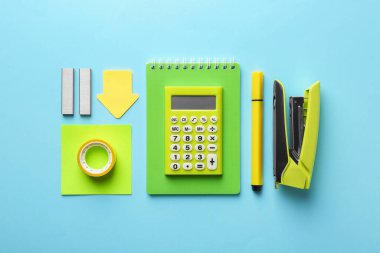 Yellow stapler and other stationery on light blue background, flat lay