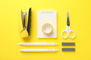 Stapler and other stationery on yellow background, flat lay