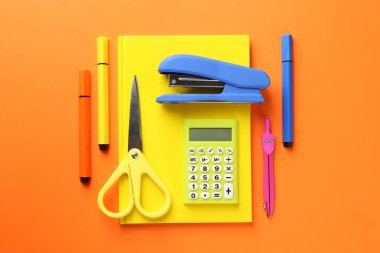Blue stapler and other stationery on orange background, flat lay