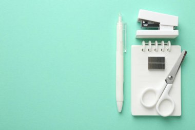 Stapler and other stationery on turquoise background, flat lay. Space for text