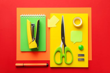 Stapler and other stationery on red background, flat lay