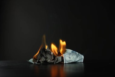 Burning dollar banknotes on black table against dark background