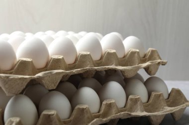 Raw chicken eggs in egg cartons on grey table, closeup