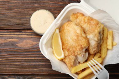 British Traditional Fish and chips with lemon and sauce on wooden table, flat lay. Space for text