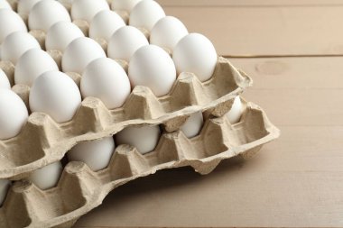 Many raw chicken eggs in cartons on wooden table, closeup