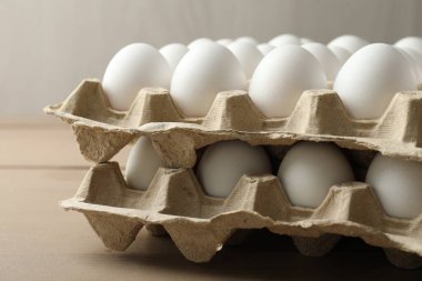 Many raw chicken eggs in cartons on wooden table, closeup