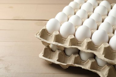 Many raw chicken eggs in cartons on wooden table, closeup. Space for text