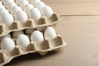Many raw chicken eggs in cartons on wooden table, closeup. Space for text