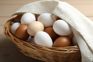 Many raw chicken eggs in wicker basket on wooden table, closeup