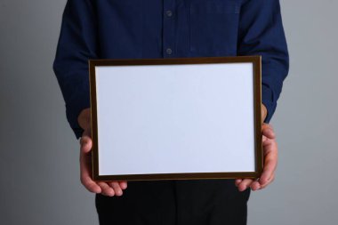 Açık gri arkaplanda boş diploma çerçevesi olan bir adam, yakın plan. Tasarım için model