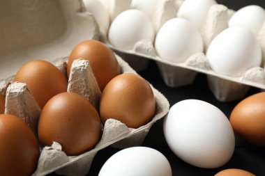 Many raw chicken eggs in cartons on black table, closeup