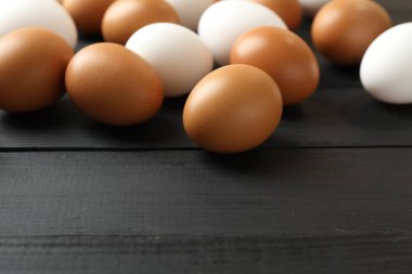 Many raw chicken eggs on black wooden table, closeup. Space for text