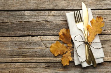 Beautiful table setting. Cutlery with napkin and autumn decor on wooden background, top view. Space for text