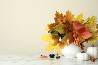 Autumn composition with vase of dry leaves, berries and decor on white marble table. Space for text