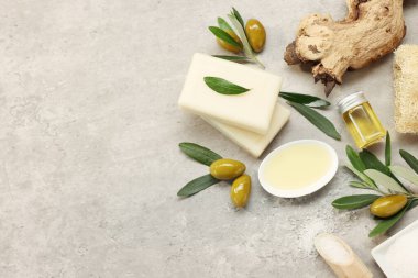 Flat lay composition with handmade soap bars, olives and oil on gray textured table. Space for text