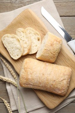 Taze çıtır ciabatalar, buğday kulakları ve tahta masa üzerinde bıçak, düz uzanmış