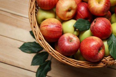Hasır sepetteki taze elmalar ve ahşap masada yeşil yapraklar, üst manzara. Metin için boşluk