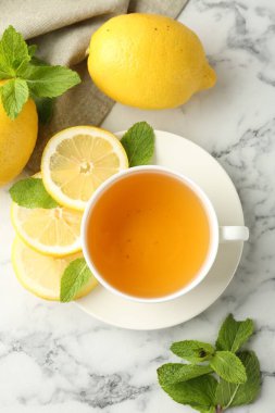 Aromatic tea in cup with lemons and mint on white marble table, flat lay