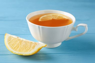 Aromatic tea in cup with lemon on light blue wooden table, closeup