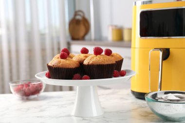 Mutfaktaki beyaz mermer masada ahududu ve hava kızartma makineli taze pişmiş muffinler.