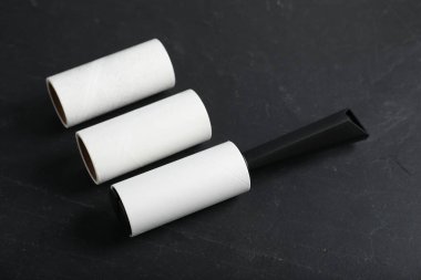 Lint roller and adhesive rolls on black table, closeup