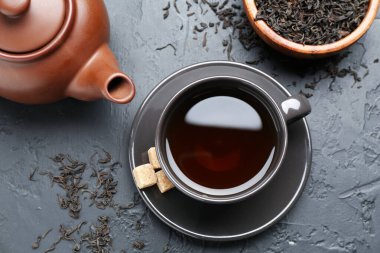 Fincanda romatik çay, kahverengi şeker, kurumuş yapraklar ve siyah masada çaydanlık.