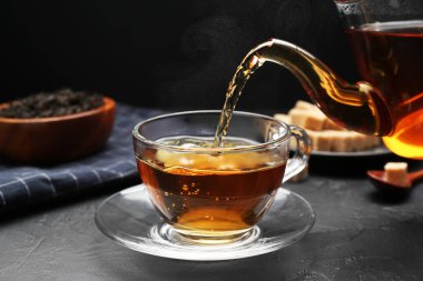 Pouring aromatic tea into glass cup at black table, closeup